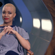 Sonequa Martin-Green with very short styled hair and wearing a striped shirt while sitting in a director's chair on the set of Star Trek: Discovery.